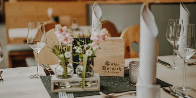Gedeckter Tisch mit Blumenvase, Gläsern und Speisekarte.
