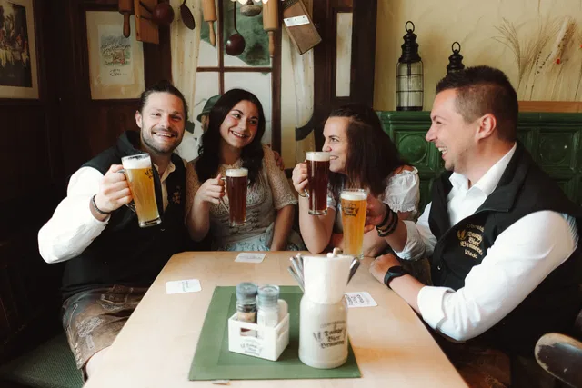 Gruppe von vier Personen in einer Kneipe stoßt an mit Bier und lächelt.