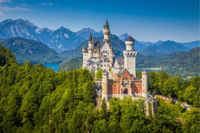 Schloss Neuschwanstein auf einem bewaldeten Hügel vor Alpenlandschaft