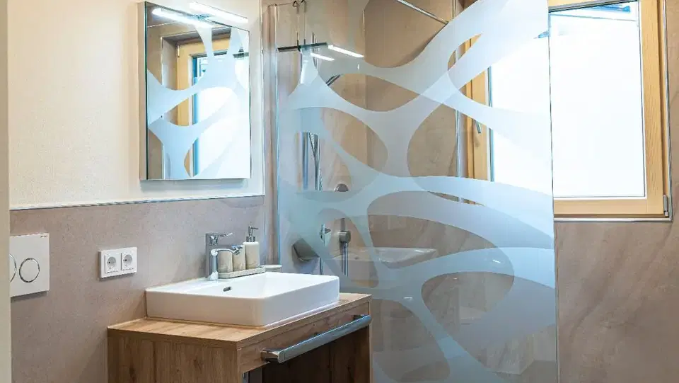 Badezimmer mit Glasduschwand, Waschtisch aus Holz und WC.