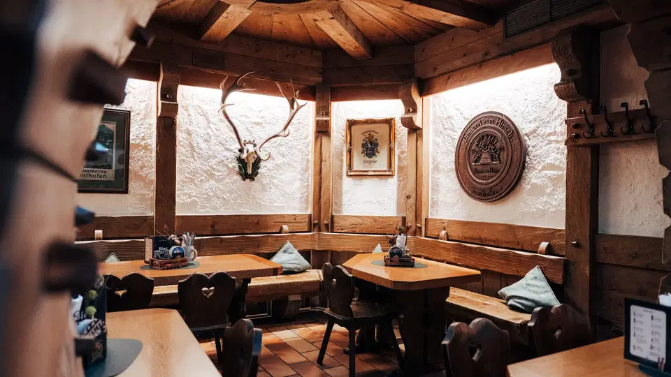 Restaurantstube mit Holzdecke, gedeckten Tischen und Hirschgeweih an der Wand