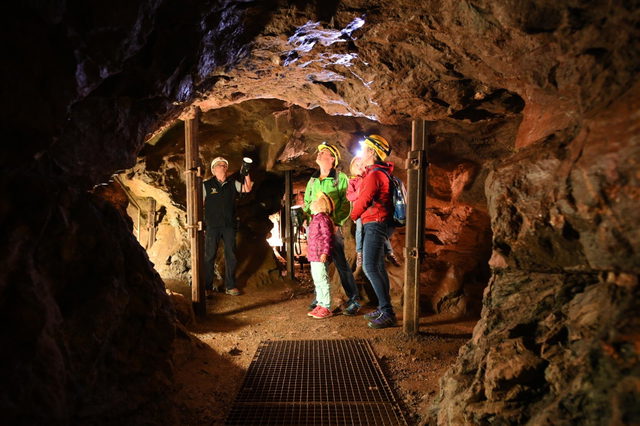 Besucher gehen mit Helmen durch einen Stollen der Erzgruben Burgberg.