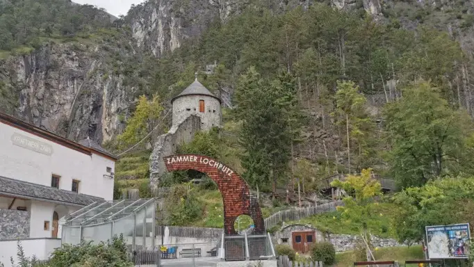 Eingang zum Zammer Lochputz mit Römerturm vor den Felswänden in Zams