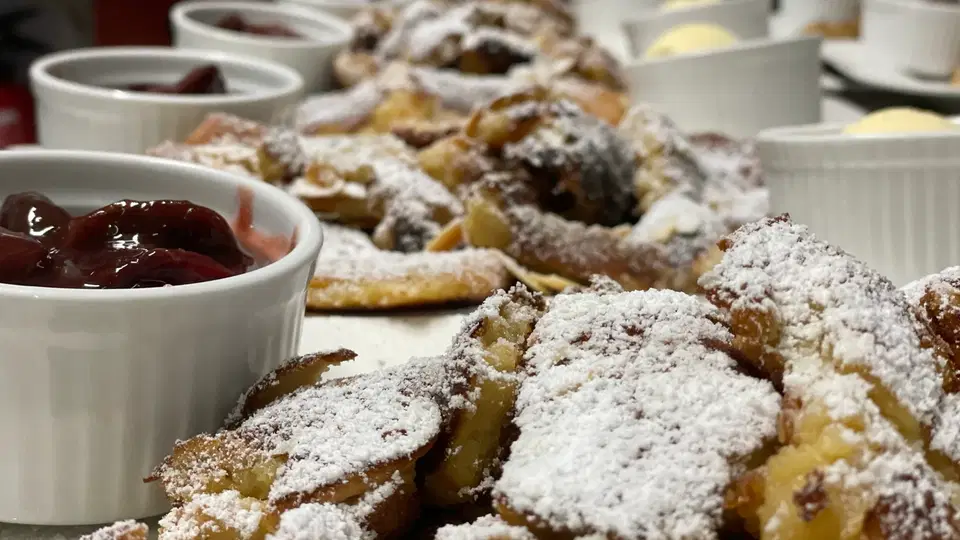 Dessert-Buffet mit gebackenen Gebäcken, Puderzucker und Fruchtkompott in Schalen.