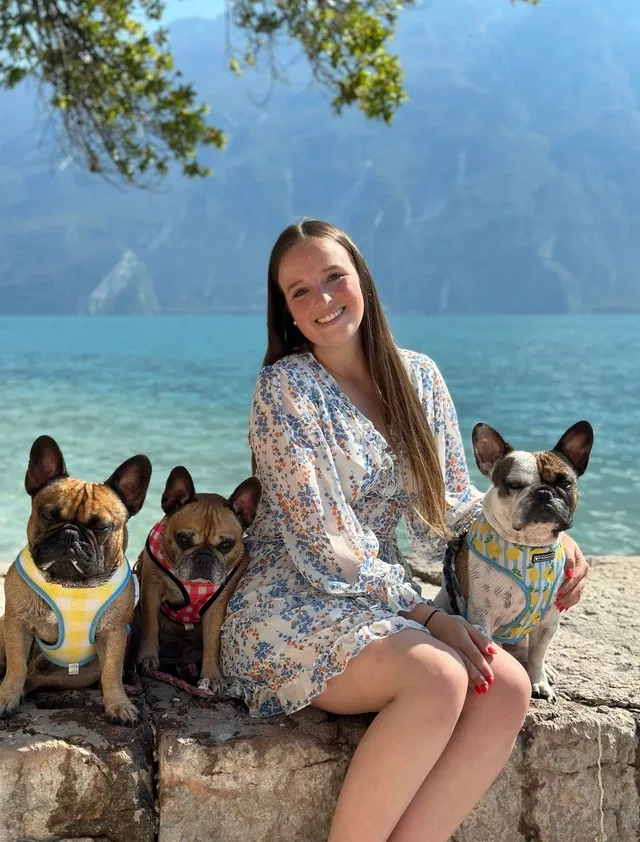 Junge Frau mit vier Hunden sitzt an einem Seeeufer.