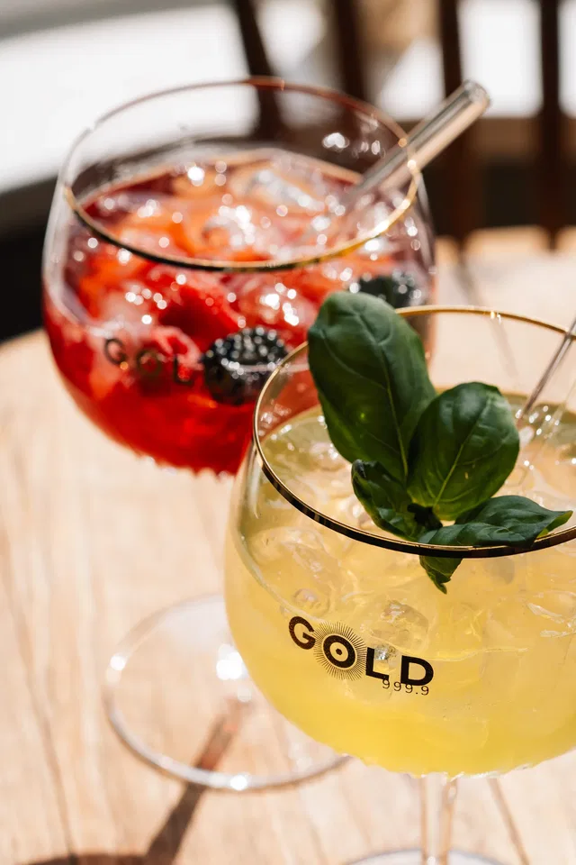Zwei Cocktails mit Eis und Beeren, Basilikum-Garnitur auf Holztisch