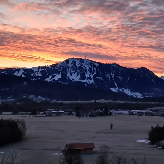 Berg mit Schneebedeckten Hängen vor rosa-orangeem Sonnenuntergang.