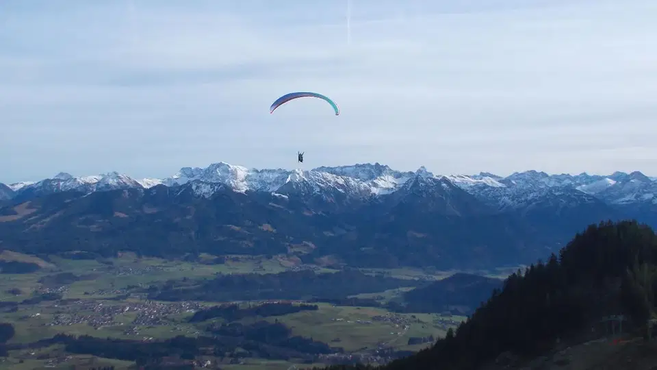 Paragleiter über einer Berglandschaft mit Schnee-Gipfeln.