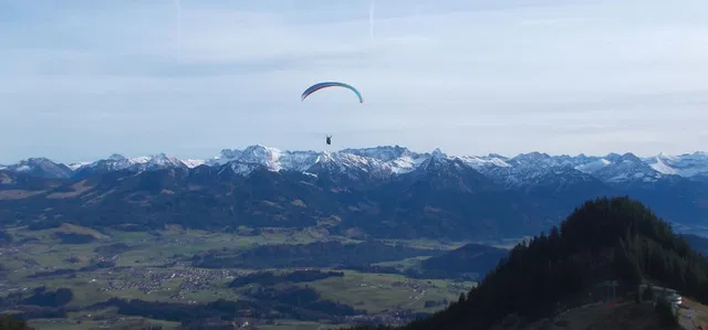 Paragleiter über einer Berglandschaft mit Schnee-Gipfeln.