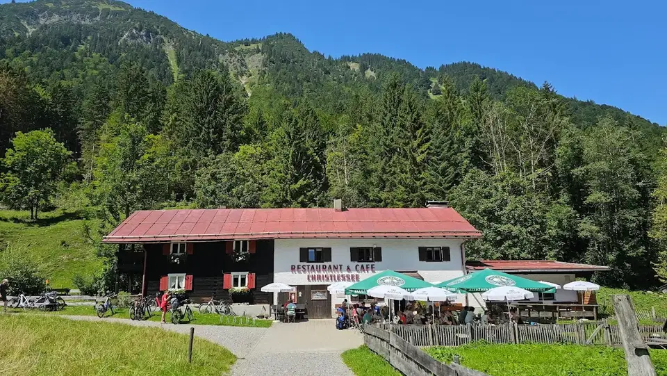 Restaurant mit rotem Dach vor Waldhügeln, Außenbereich mit Tischen und grünen Sonnenschirmen