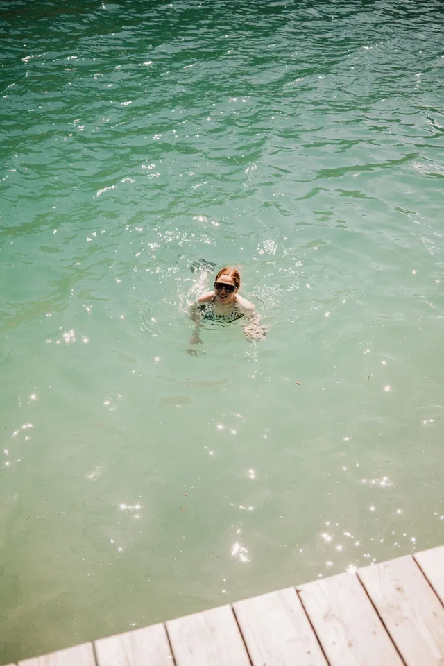 Person schwimmt im türkisfarbenen Wasser nahe dem Holzsteg.
