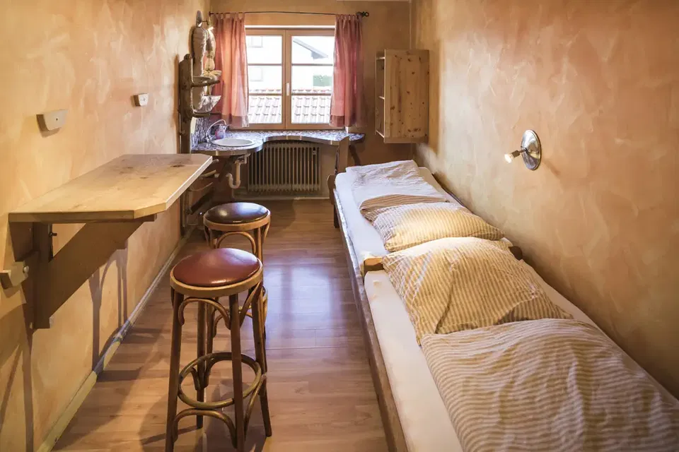 Zimmer Hans mit zwei hintereinander stehenden Einzelbetten und Tisch am Fenster