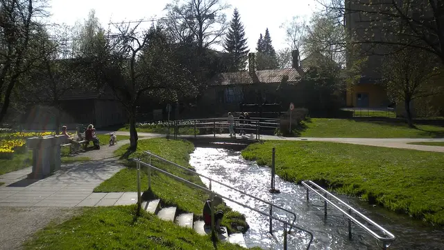 Grünanlage im Stadtpark Neue Welt in Memmingen mit Wasserlauf, Fußweg, kleiner Brücke und Bäumen. Ortsmotiv zur Ausflugsplanung.
