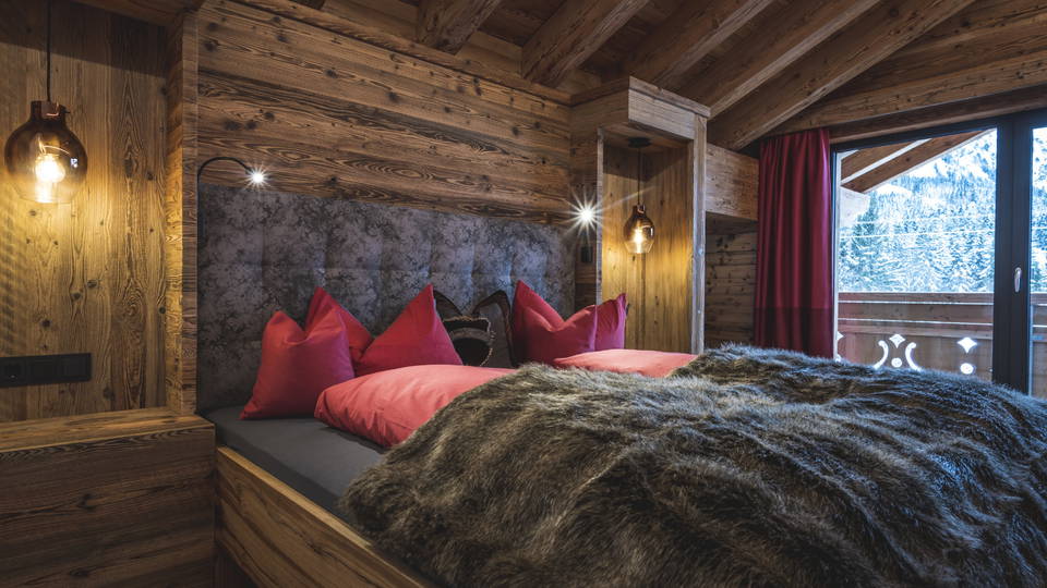 Schlafzimmer mit Doppelbett, Holzwänden und roten Kissen