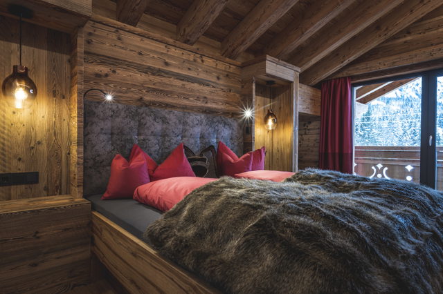 Schlafzimmer mit Doppelbett, Holzwänden und roten Kissen