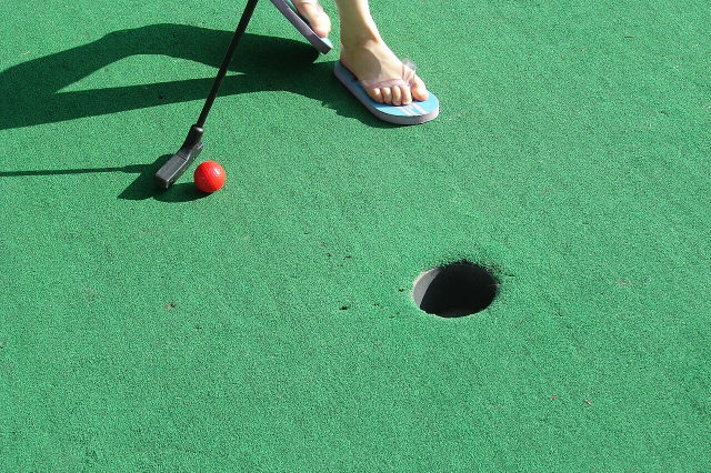 Symbolbild: Minigolfball und Schläger auf einer Minigolfbahn