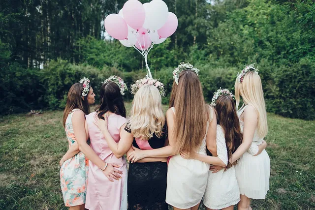 Eine Gruppe mit Blumenkränzen und Luftballons steht im Grünen.