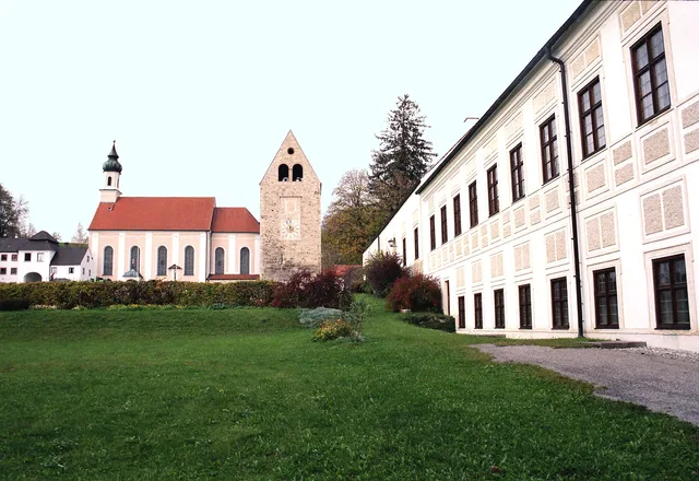 Historische Anlage mit Kirchturm, rotem Dach und langem weißen Gebäudekomplex am Grünstreifen