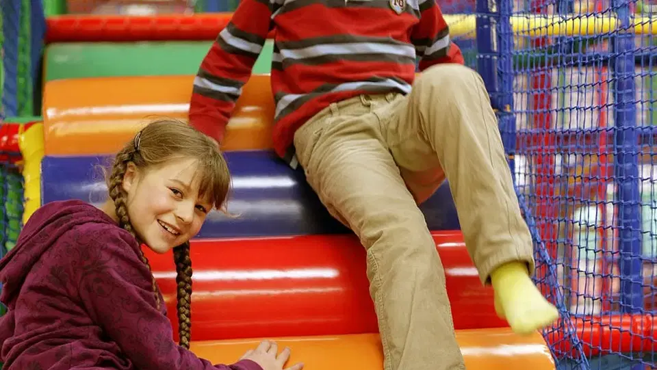 Zwei Kinder auf bunten gepolsterten Stufen eines Indoor-Spielbereichs.