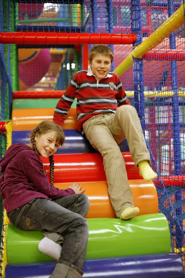 Zwei Kinder auf bunten gepolsterten Stufen eines Indoor-Spielbereichs.
