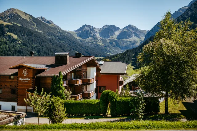 Alpenhotel Alpenstube mit Holzfassade vor Bergpanorama und grünen Gärten.