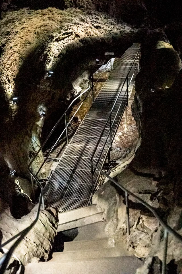 Metallsteg durch eine Höhle mit Felswänden und Geländern.