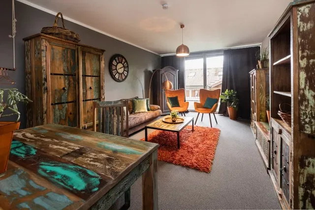 Rustikales Wohnzimmer mit vintage Holzschränken, orange Teppich, zwei orange Sessel, Couchtisch undP
