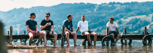 Fünf Menschen sitzen auf einem Steg mit den Füßen im Wasser
