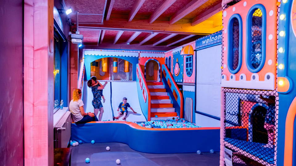 Bunt beleuchteter Indoor-Spielplatz mit Bällebad, Treppe und Kletterelementen