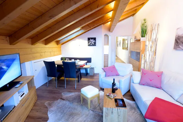 Gemütliches Dachgeschoss-Wohnzimmer mit Holzbalken, Sofa, Sessel, Esstisch und Fernseher.
