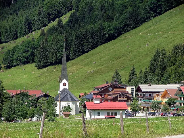 Kirche mit spitzer Turmspitze in einem Bergdorf vor grüner Hügellandschaft.