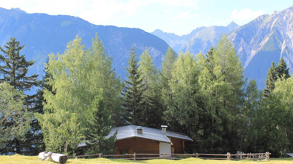 Blick vom Venet über Almwiesen und eine Holzhütte zu den umliegenden Bergen