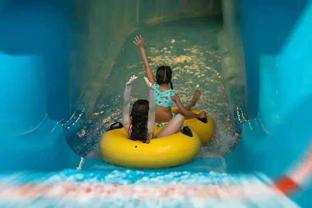 Zwei Kinder auf gelben Reifen-Tubes rutschen eine blaue Wasserrutsche hinunter.