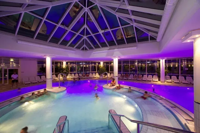 Beheiztes Innenbad mit kreisförmigem Pool, Glasdach, umlaufenden Sitzgelegenheiten und lila Beleucht