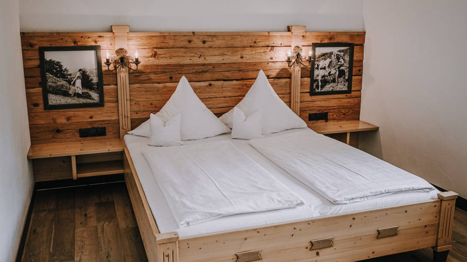 Doppelbett vor Holzwand mit Bergbildern im Zimmer Edelweiß.