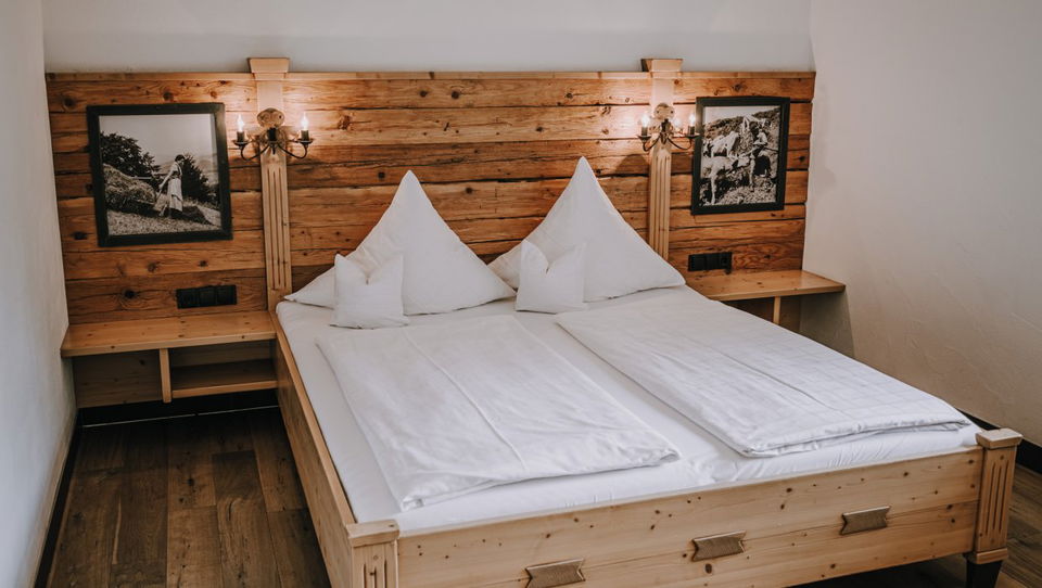 Doppelbett vor Holzwand mit Bergbildern im Zimmer Edelweiß.