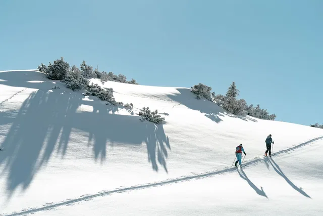 Zwei Wintersportler auf Skitour im verschneiten Hang bei klarem Himmel