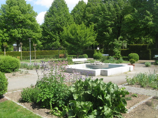 Grüner Kurpark in Bad Abbach mit Brunnen, Blumen und Sitzbänken.