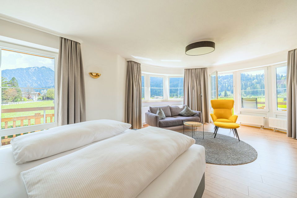 Helles Zimmer mit Bett, Sofa, gelbem Sessel und Bergblick