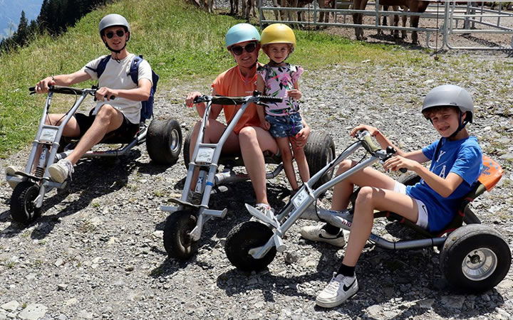 Drei Mountaincarts mit Helmtragenden, ein Kind fährt bei einem Erwachsenen mit