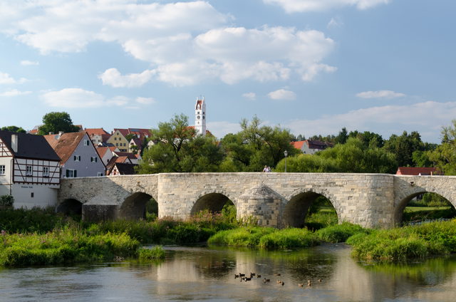 Steinbogenbrücke über die Wörnitz in Harburg mit Häusern, Kirchturm und Enten im Wasser