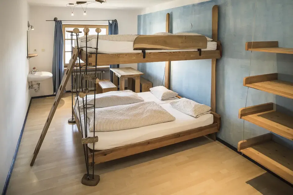 Zimmer Ocean mit Holzstockbett, Leiter und Regalen vor blauer Wand