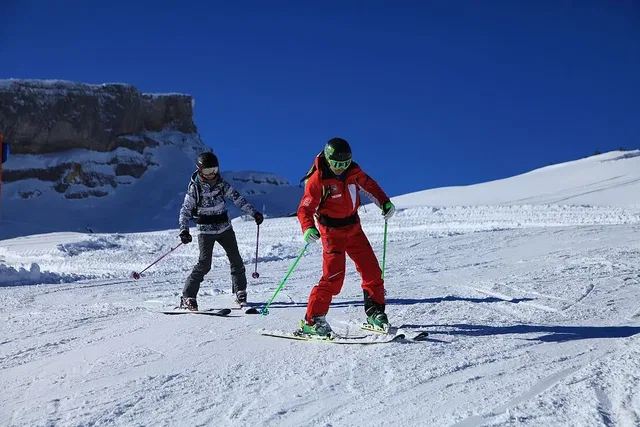 Zwei Skifahrer in Winter-Outfits fahren bergab auf einer schneebedeckten Piste.