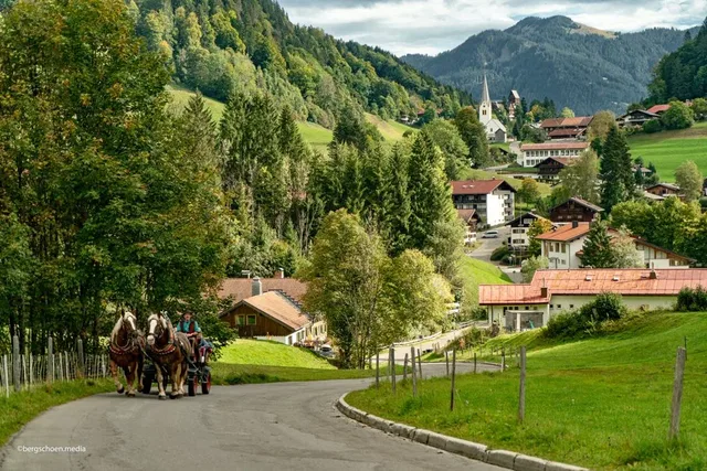 Pferdekutsche auf einer Straße vor einem Dorf mit Kirche.