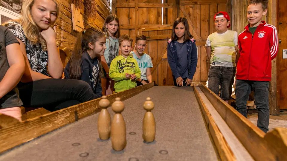 Gruppe von Kindern spielt Kegeln an einer Holzbahn in einer Holzhütte.