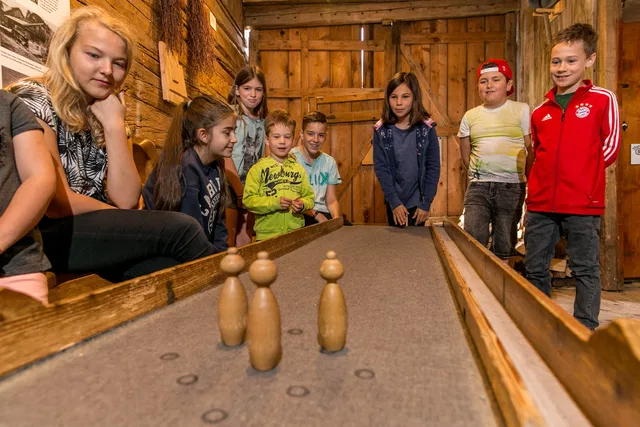 Gruppe von Kindern spielt Kegeln an einer Holzbahn in einer Holzhütte.