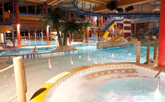 Innenwasserpark mit Becken, Rutschen, Whirlpool, künstlichen Palmen und bunten Strukturen.
