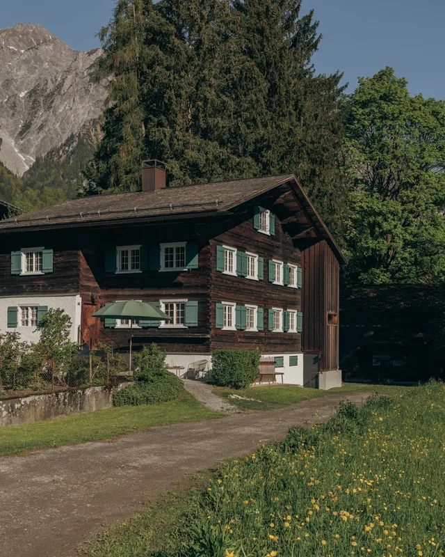 Traditionelles Chalet mit grünen Fensterläden vor Wald und Bergen