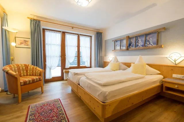 Schlafzimmer mit Holzbett, gemütlicher Sitzerunde und Balkontüren