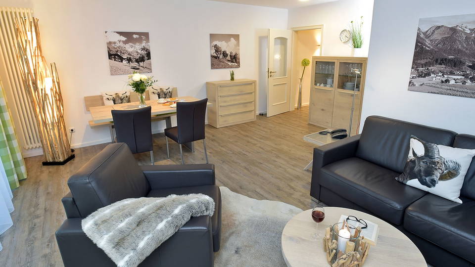 Wohn- und Esszimmer der Ferienwohnung Biberkopf mit dunkler Ledersitzgruppe und Holzmöbeln.